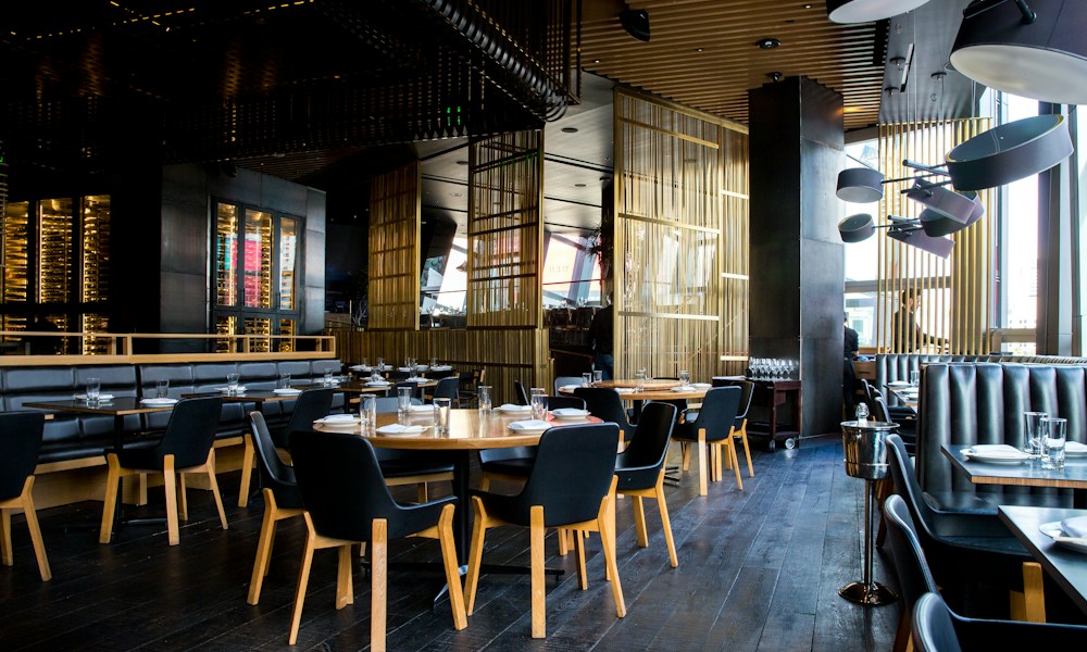 Ahşap masaları ve sıcak aydınlatmasıyla akşam yemeğine hazırlanmış bir restoran